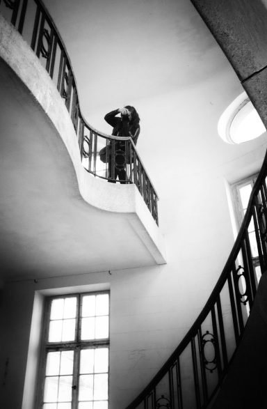 Eine Person in einem langen Mantel steht auf einer Treppe mit geschwungem Geländer.